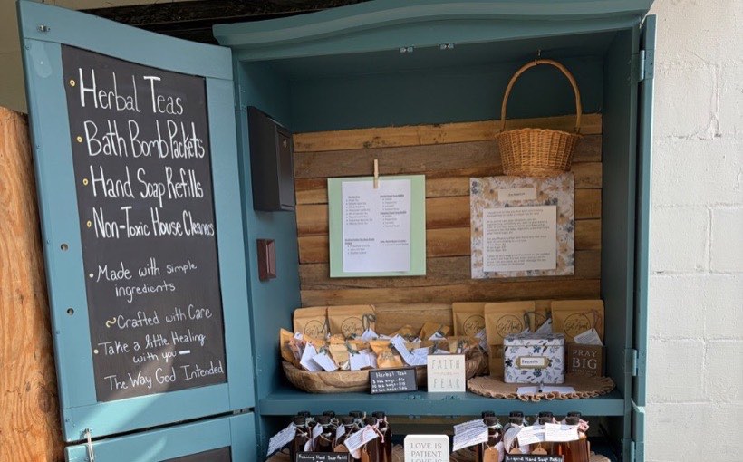 The Set Apart stand: a teal cabinet with chalkboard doors, kraft tea packets and amber soap bottles on its shelves.